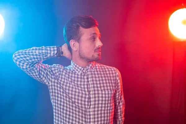 Encantador joven hipster sonriente hombre está posando sobre el fondo de la iluminación del estudio rojo y azul. Concepto de hombre pensativo . — Foto de Stock