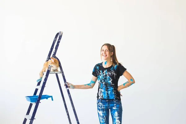 Jonge vrouw kunstschilder, ontwerper en werknemer schildert de muur. De kat zit volgende op de ladder en kijkt naar het werk. — Stockfoto