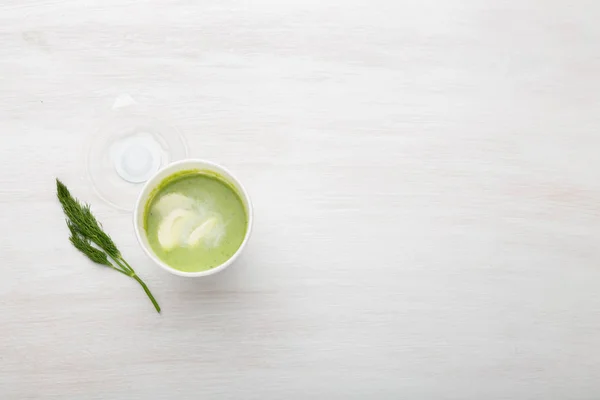 Чашка зеленого супа с кусочками овощей лежит на белом столе с зеленым горошком. Концепция здорового питания. Копирование пространства — стоковое фото