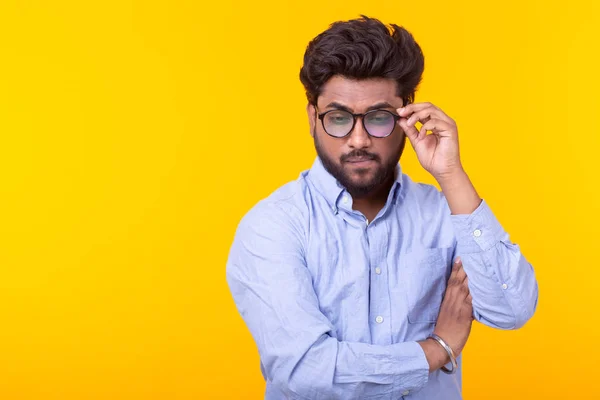 Young male professor with a beard in glasses and formal clothes is looking down thoughtfully posing on a yellow background. Concept of search and selection. Copy space