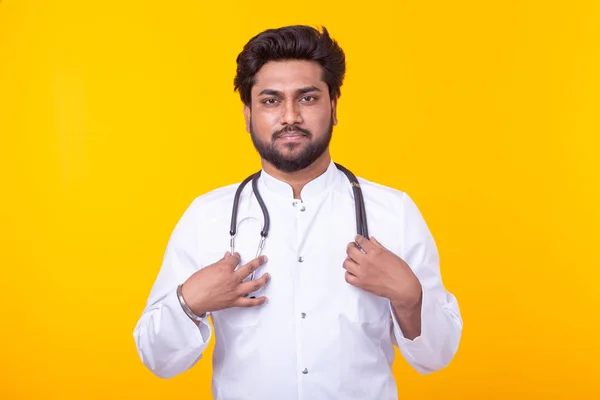노란색 배경에 포즈를 취한 청진기를 가진 흰색 코트를 입은 긍정적 인 젊은 인도 의사. 효과적인 의학 및 의사 조언의 개념. — 스톡 사진