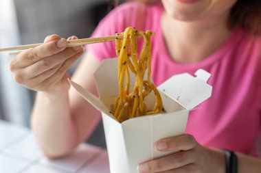 Bir kafede oturan ahşap çubuklarla udon erişte si yiyen kimliği belirsiz genç bir kızın elini kapatın. Asya mutfağı konsepti.