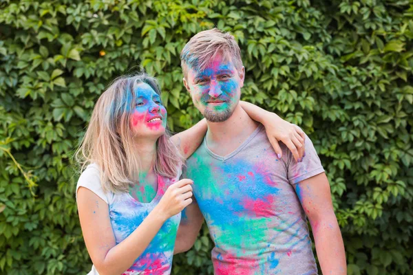 Conceito de férias, holi e pessoas - Mulher sorridente e homem posando com pó multicolorido em seus rostos — Fotografia de Stock