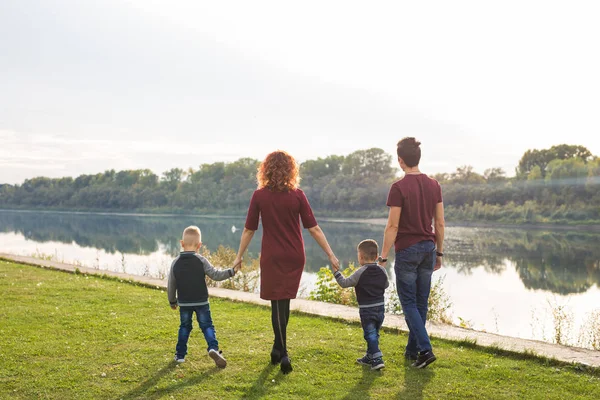 Parenthood and nature concept -Family of mother and father with two boys twins kids in a park at summer by a river at sunny day — Stock Photo, Image