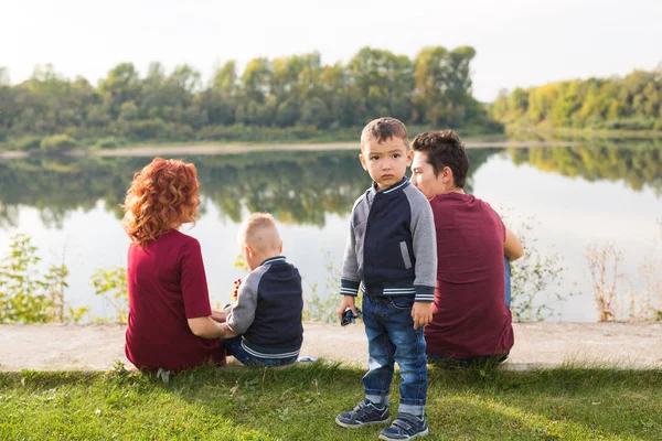 Föräldraskap, natur, människor koncept - familj med två söner sitter nära sjön — Stockfoto