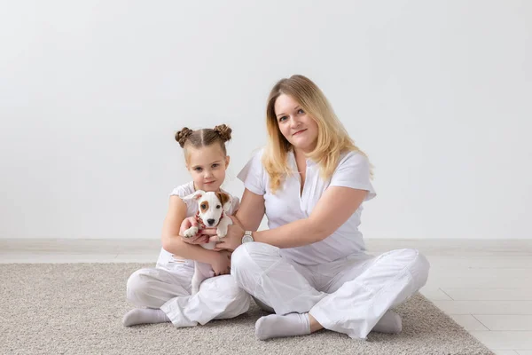 people, family and pets concept - mother and daughter sitting on the floor with puppy Jack Russell Terrier