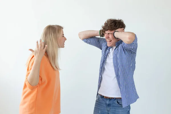 Young nervous couple wicked cute girl and upset young guy plugging ears cursing standing against white background. Misunderstanding and relationship crisis concept.