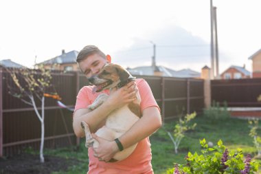 Sakallı pozitif genç adam sevgili köpeği Jack Russell Terrier tutuyor ve güneşli bir yaz gününde onun kır evinin bahçesinde ortak bir dinlenme tadını çıkarıyor. Onların dört için aşk kavramı