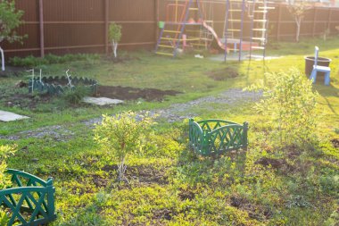 Yeşil çim ve çalılar ve küçük oyun alanı ile güneşli bahçe