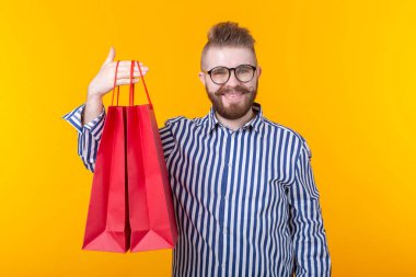 Neşeli genç hipster sarı bir arka planda kırmızı alışveriş torbaları tutuyor. Süpermarket ve hediyeler alışveriş kavramı. Reklam alanı.