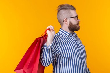 Neşeli genç hipster sarı bir arka planda kırmızı alışveriş torbaları tutuyor. Süpermarket ve hediyeler alışveriş kavramı. Reklam alanı.