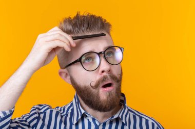 Bir bıyık ve sakal sarı bir arka plana karşı saçını tarak ile komik yakışıklı genç erkek hipster portresi. Berber Atölyesi konsepti ve öz bakım.