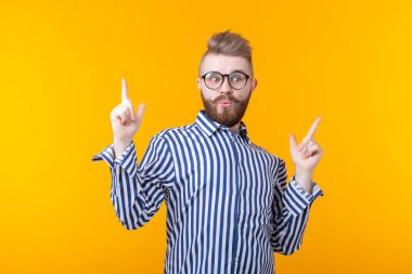 Bıyıklı ve sakallı pozitif genç adam mutlu bir şekilde parmağını yukarı doğru işaret ediyor ve sarı bir arka plan üzerinde yararlı bir şey gösteriyor. Önemli bilgi kavramı.