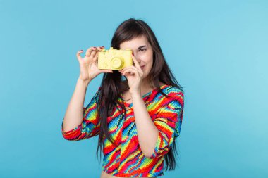 Gülümseyen genç kadın elinde kopya alanı ile mavi bir arka plan üzerinde poz sarı bir vintage kamera modeli tutuyor. Amatör ve profesyonel fotoğrafçılık kavramı.