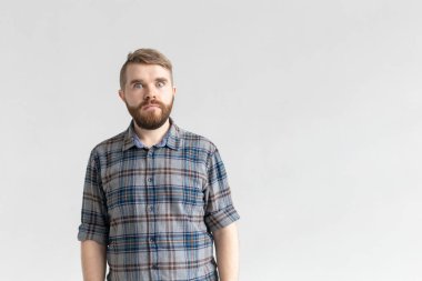 Bıyıklı ve sakallı yakışıklı adam, beyaz arka plana karşı sürpriz bir şekilde şişkin gözler yapıyor. Sürpriz ve belirsizlik kavramı.