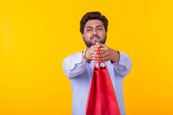 Un indio con barba sostiene bolsas rojas posando sobre un fondo amarillo. Concepto de supermercado . — Foto de Stock