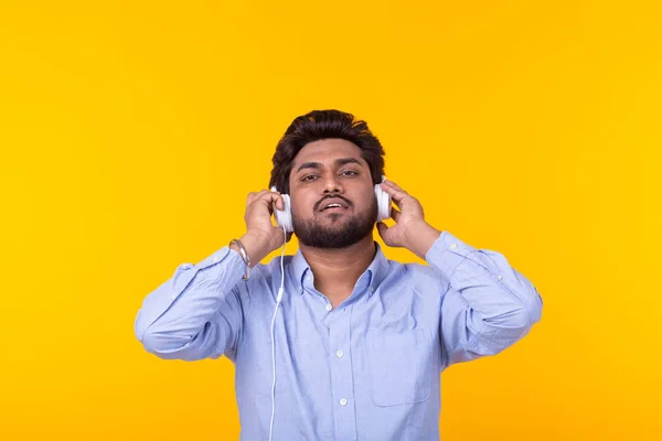 Bonito homem indiano relaxado com barba está ouvindo música favorita nos fones de ouvido em fundo amarelo. Conceito de assinatura de música e rádio online . — Fotografia de Stock