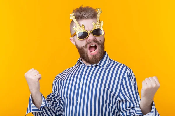 Joven positivo con gafas en forma de guitarras se regocija sobre un fondo amarillo. El concepto de celebración y fiestas . — Foto de Stock