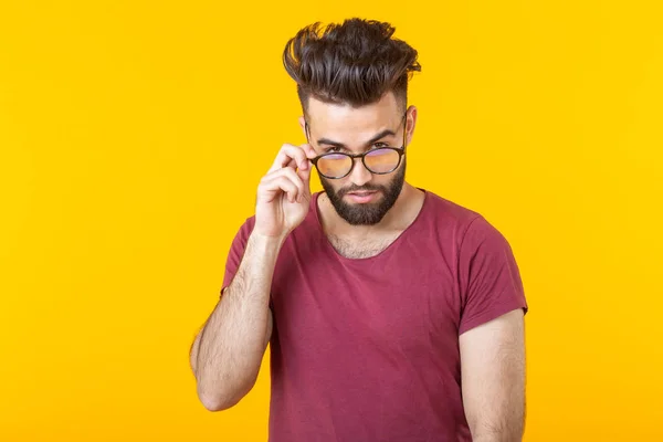 一个英俊的年轻男性嬉皮士戴着眼镜，留着胡须，在黄色背景上周到地看着相机的肖像。选择概念和广告 — 图库照片