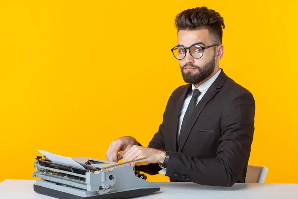 Ung flot mandlig forretningsmand i formelt tøj, der skriver tekst på en skrivemaskine, der poserer på gul baggrund. Plads til reklame. Erhvervskoncept . - Stock-foto