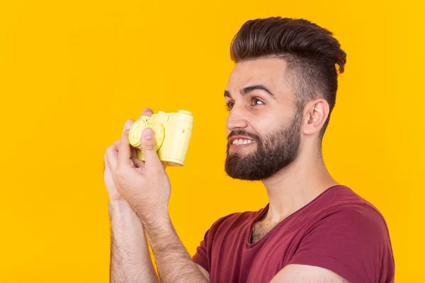 Positive young hipster man with a beard holding a yellow vintage camera posing on a yellow background. Concept of hobby and professional photography — Stock Photo, Image