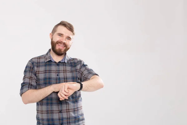 Hombre barbudo feliz en camisa a cuadros apuntando en el reloj de pulsera sobre fondo blanco con espacio de copia — Foto de Stock