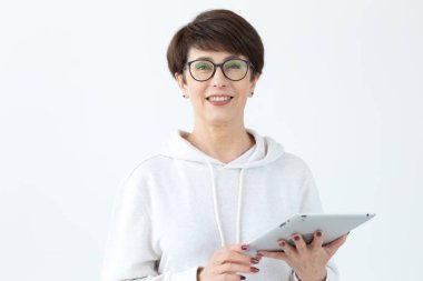 Rahat giysiler içinde Sevimli orta yaşlı kadın beyaz bir arka plan üzerinde bir tablet kullanarak online mağazalar arıyor. Kablosuz internet ve online alışveriş kavramı. Copyspace.