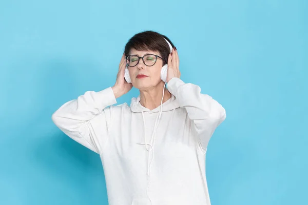 Beautiful middle-aged woman in a white sweater and glasses is listening to music while posing on a red-blue background in a studio. The concept of a favorite hobby. Advertising space. — Stock Photo, Image