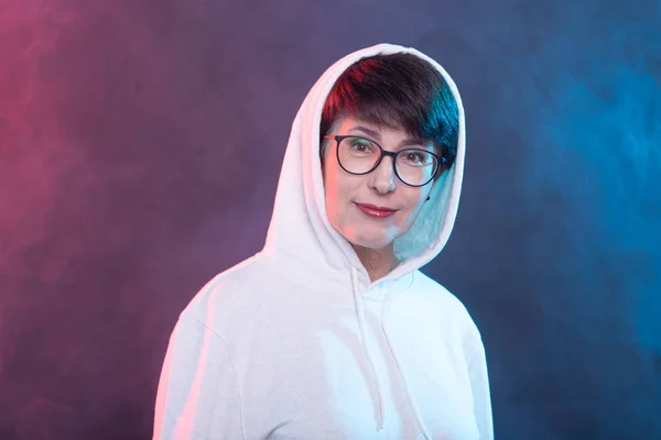 Portrait of a cheerful pretty woman in a light sweater and glasses posing on a blue background. The concept of a positive middle-aged woman. Advertising space. — Stock Photo, Image