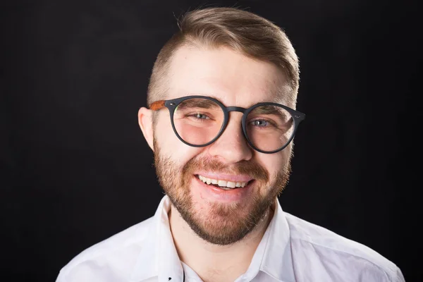 Retrato de joven hombre barbudo riendo y en gafas sobre el fondo negro — Foto de Stock