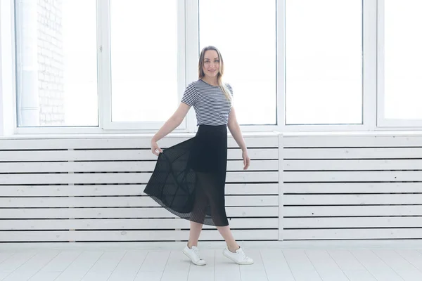 Молодежь, стиль и люди концепция - молодая женщина в черной юбке и кроссовки, стоящие у окна — стоковое фото