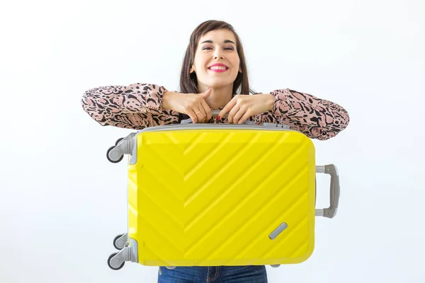 Mujer joven de pie con una maleta amarilla sobre el fondo de una pared blanca con espacio para copiar. El concepto de nuevos descubrimientos y la disponibilidad de viajes . — Foto de Stock