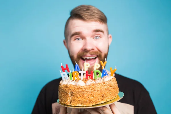 Crazy vicces pozitív fickó csípő tartó boldog születésnapi torta a kezében állt a kék háttérben. Fogalma viccek és üdülési üdvözletek. — Stock Fotó