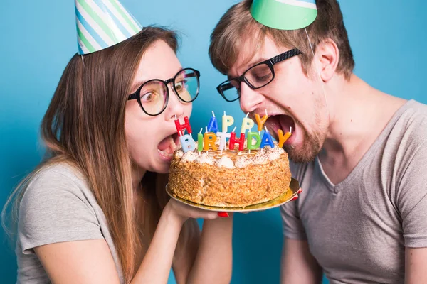 Primer plano de la extraña joven pareja chica y niño en sombreros de papel quieren morder un pedazo de pastel de felicitación. Cumpleaños y concepto de felicitaciones . —  Fotos de Stock