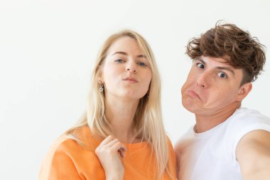 Büyüleyici genç çift sevimli sarışın kız beyaz arka plan üzerinde poz bir selfie çekmek. Kavram genç bir çift gençler veya bin yıllık aşık.