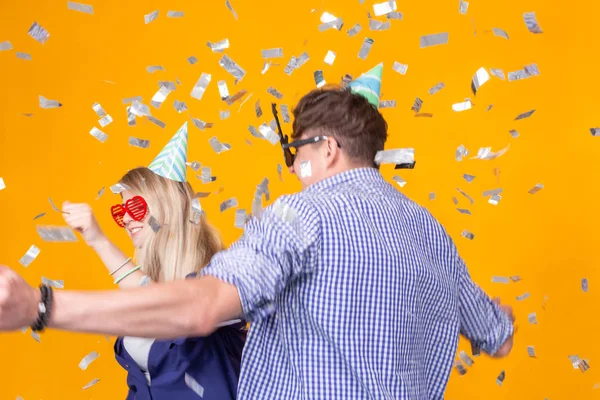Divertimento, feriados e conceito de festa - Casal dançando entre confetes caindo no fundo amarelo — Fotografia de Stock