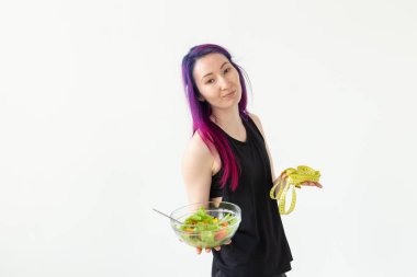 Renkli saçlı ince genç asya kız bir ölçüm bandı tutar ve elinde beyaz bir arka plan üzerinde poz hafif bir sebze salatası tutan. Sağlıklı beslenme konsepti. Copyspace.