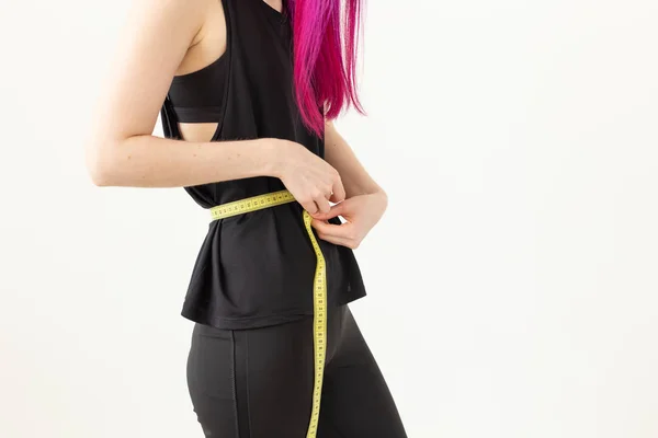 Neidentifikovaná mladá dívka alternativců s purpurovými vlasy měří její pas s měřicí páskou na bílém pozadí. Koncepce zdravého životního stylu. Prostor pro reklamu. — Stock fotografie