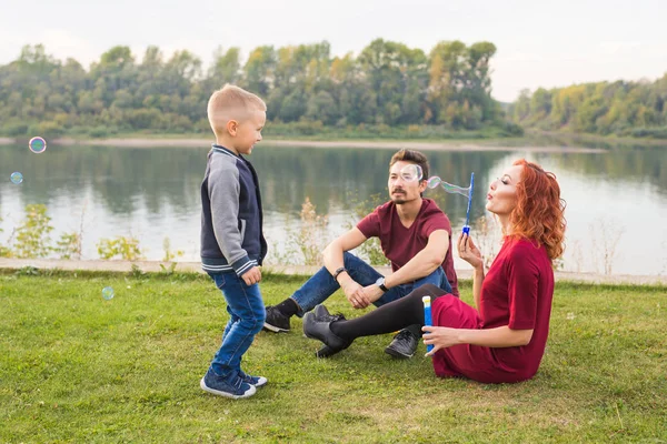 Familjen och naturen koncept - mamma, pappa och deras barn som leker med färgglada såpbubblor — Stockfoto