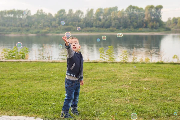 Children and nature concept - Boy trying to catch soap bubbles — Stock Photo, Image