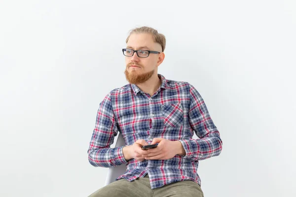 Молодой бородатый хипстер сидит на белом фоне с копировальным пространством — стоковое фото