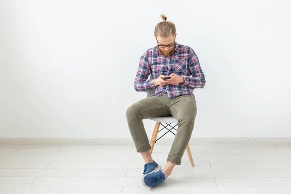 Hombre guapo barbudo en camisa a cuadros mirando el teléfono celular sobre fondo blanco — Foto de Stock