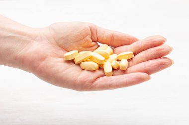 Kadın el bir kavanoz yanında beyaz bir masa arka plan üzerinde sarı hap tutar. İyileşme ve önleme nin tedavisi kavramı