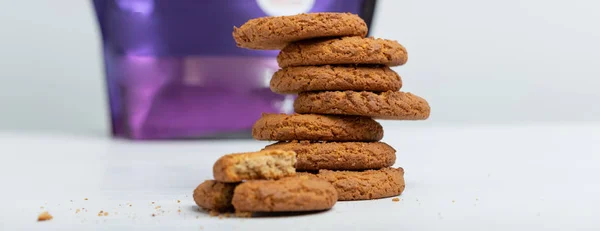 Stack of oatmeal cookies lies against the background of a packet of protein on a white table. Sports nutrition concept.