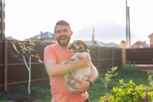 Pessoas, animais de estimação e cães conceito - jovem abraçando engraçado Jack Russell Terrier ao ar livre — Fotografia de Stock