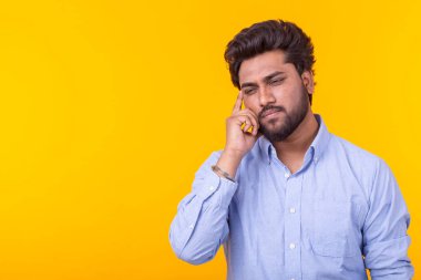 Sarı bir arka plan üzerinde poz mavi gömlek sakallı şık üzgün kalemli hint genç adam. Reklam için yer. Düşünme kavramı.