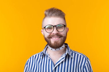 Sarı bir arka planda poz gömlek bıyık sakal ve fetiş kolye ile genç pozitif trendy adam hipster. Rock ve alt kültür konsepti.