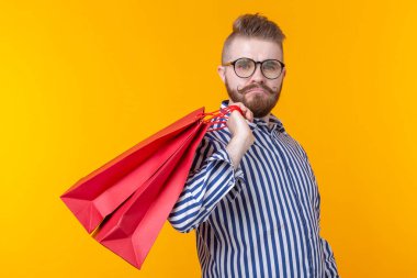 Neşeli genç hipster sarı bir arka planda kırmızı alışveriş torbaları tutuyor. Süpermarket ve hediyeler alışveriş kavramı. Reklam alanı.