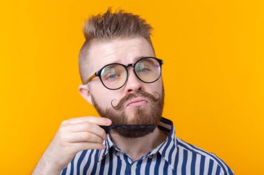 Bir bıyık ve sakallı bir sarı arka planda bıyığını tarıyor komik yakışıklı genç erkek hipster bir portre. Berber ve güzellik konsepti.