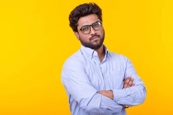 Jovem professor indiano, com barba em óculos e roupas formais está olhando para baixo pensativo posando em um fundo amarelo. Conceito de busca e seleção. Espaço de cópia — Fotografia de Stock